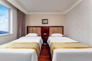 A hotel room with two beds, a wooden headboard, a small window, and a door.