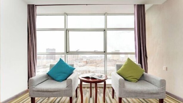 Une chambre d’hôtel avec deux fauteuils, une petite table ronde et une grande fenêtre avec des rideaux.