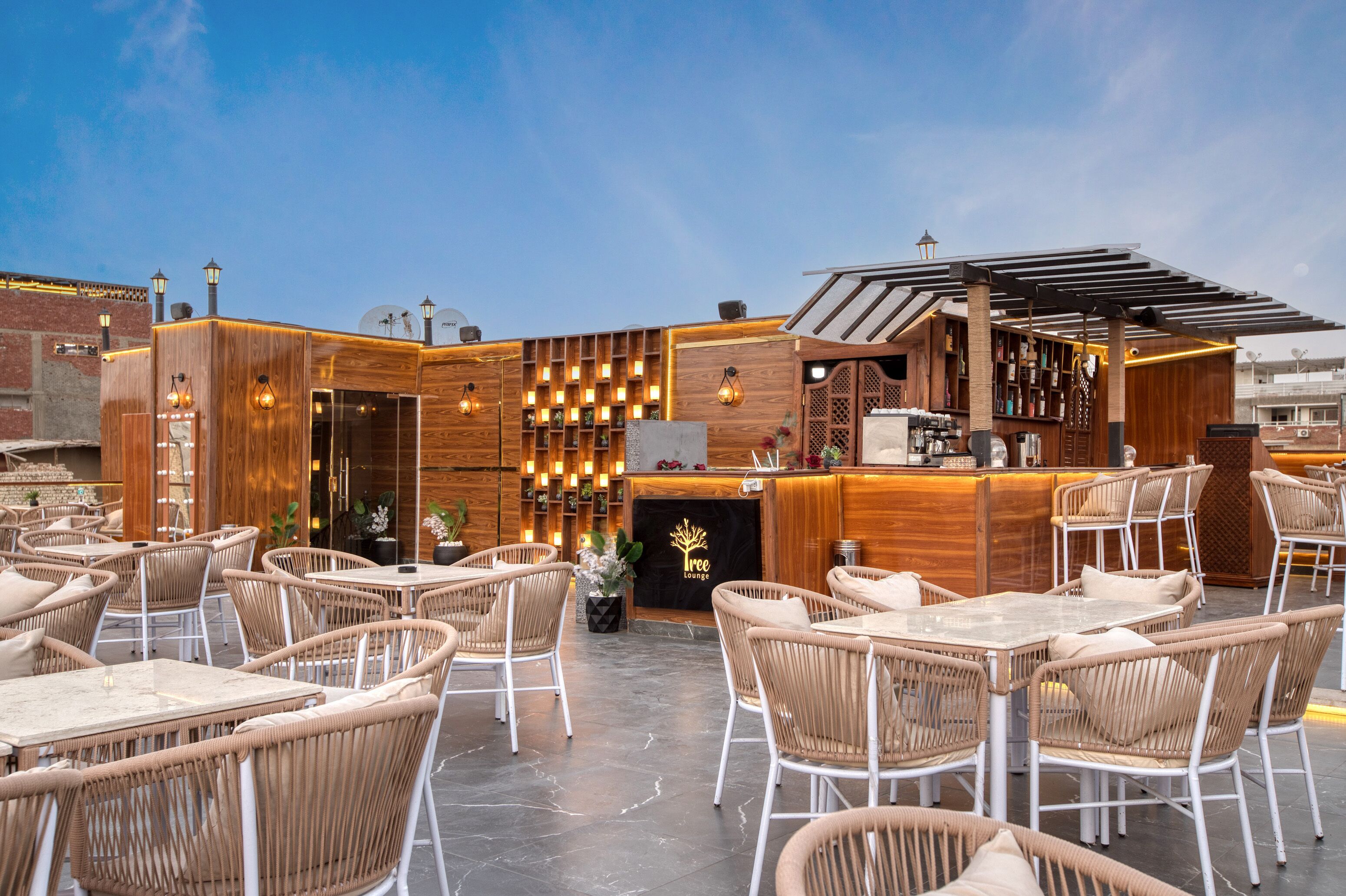 An outdoor seating area with wicker chairs and tables, a bar with a wooden counter, and a sign that reads "Tree Lounge".