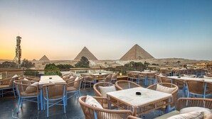 An outdoor seating area with wicker chairs and tables, overlooking the pyramids. - Shadow Pyramids View INN (Giza)
