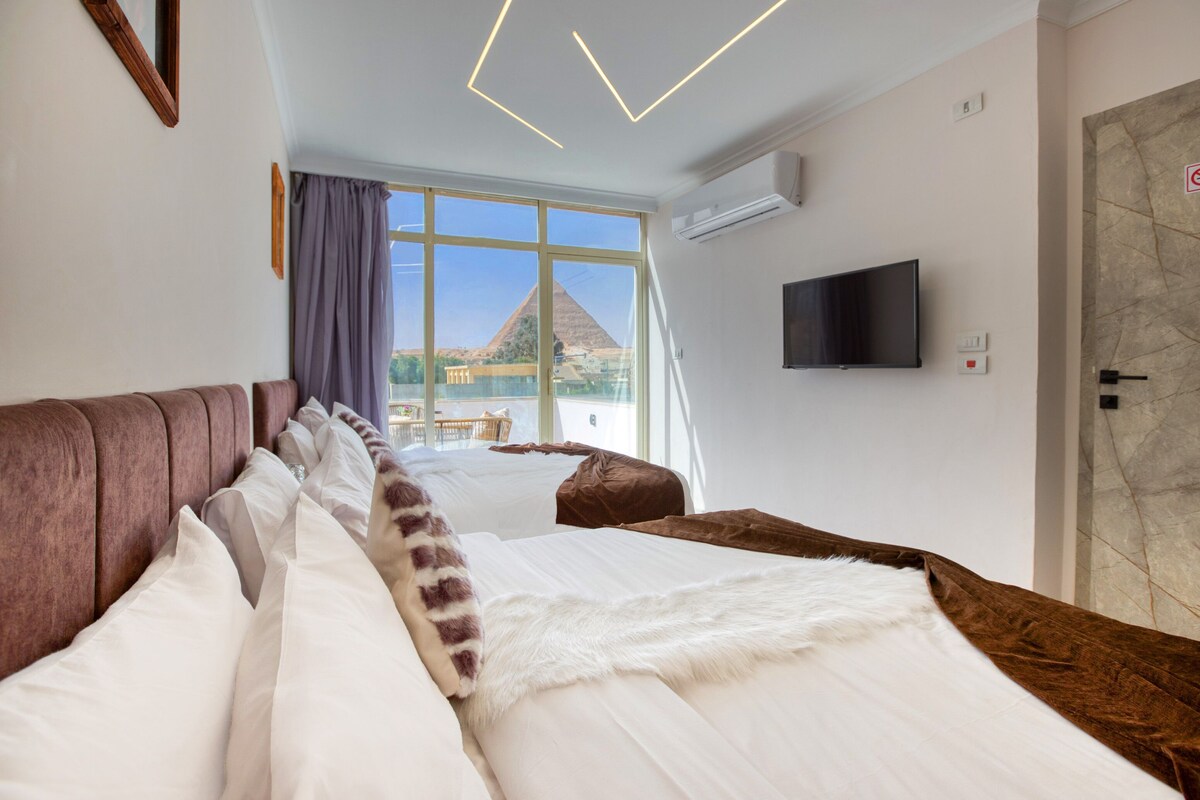 Habitación de hotel con dos camas, un televisor y vista a una pirámide.