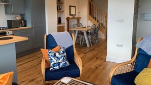 Eine moderne Küche mit grauen Schränken, einer Holz Arbeitsplatte und einer Mikrowelle. Ein Essbereich mit Tisch und Stühlen, und eine Treppe, die zu einer weiteren Ebene führt.
