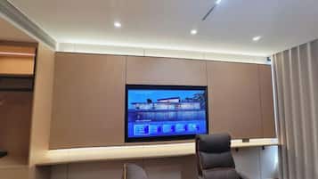 A modern hotel room with a large flat-screen TV mounted on the wall, a comfortable seating area with a sofa and chairs, and a wooden side table.