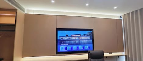 A modern hotel room with a large flat-screen TV mounted on the wall, a comfortable seating area with a sofa and chairs, and a wooden side table.