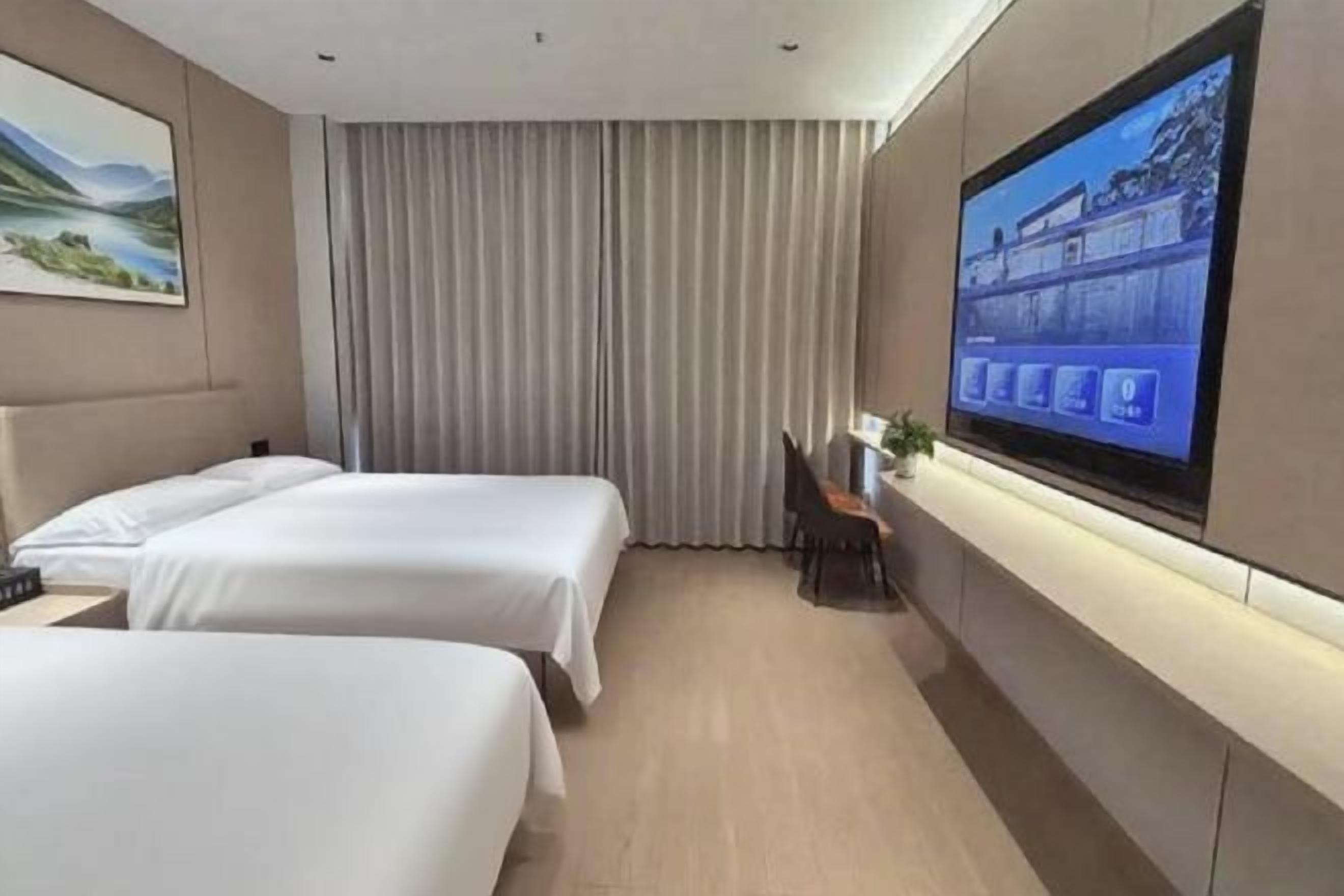 A hotel room with two beds, a TV on the wall, a curtain, and a desk with a chair.