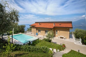 Ein zweistöckiges Haus mit Swimmingpool, einer Terrasse mit Gartenmöbeln und Blick auf das Meer.