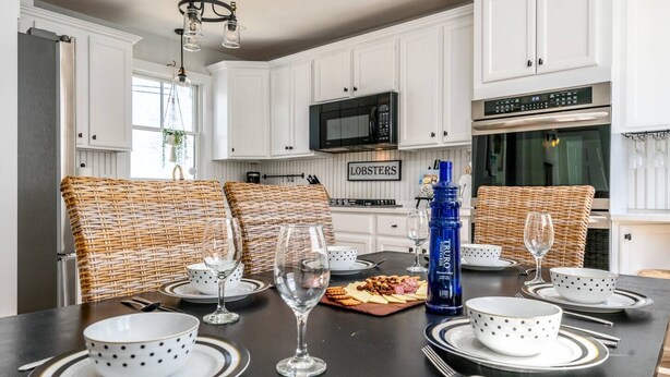 A dining area with a black table set for four, white polka-dotted bowls, clear wine glasses, and wicker chairs. - Steps to Harbor & Dining! Updated Home Slps 12 (Hyannis)