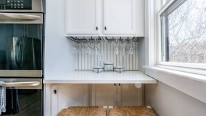 A kitchen with white cabinets, a built-in wine rack, and a small dining table with woven placemats. - Steps to Harbor & Dining! Updated Home Slps 12 (Hyannis)