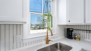A modern kitchen with white cabinetry, a stainless steel sink, and a hanging plant by the window. - Steps to Harbor & Dining! Updated Home Slps 12 (Hyannis)