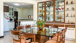 A dining area with a glass-top table surrounded by wooden chairs, a potted plant, and a kitchen in the background. - Refúgio Mirante da Lagoa - Floripa (Florianópolis)