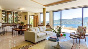 A spacious living room with a sofa, coffee table, and a view of the sea. - Refúgio Mirante da Lagoa - Floripa (Florianópolis)