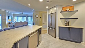 A modern kitchen with a built-in refrigerator, a coffee maker on a shelf, and a dining area with a large window. - Amazing Villa w/ Beautiful Views from Balcony! (Hilton Head Island)