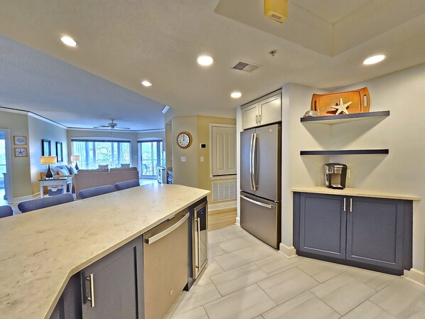 A modern kitchen with a built-in refrigerator, a coffee maker on a shelf, and a dining area with a large window. - Amazing Villa w/ Beautiful Views from Balcony! (Hilton Head Island)