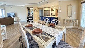 A dining area with a glass table, white chairs, and a kitchen in the background. - Amazing Villa w/ Beautiful Views from Balcony! (Hilton Head Island)