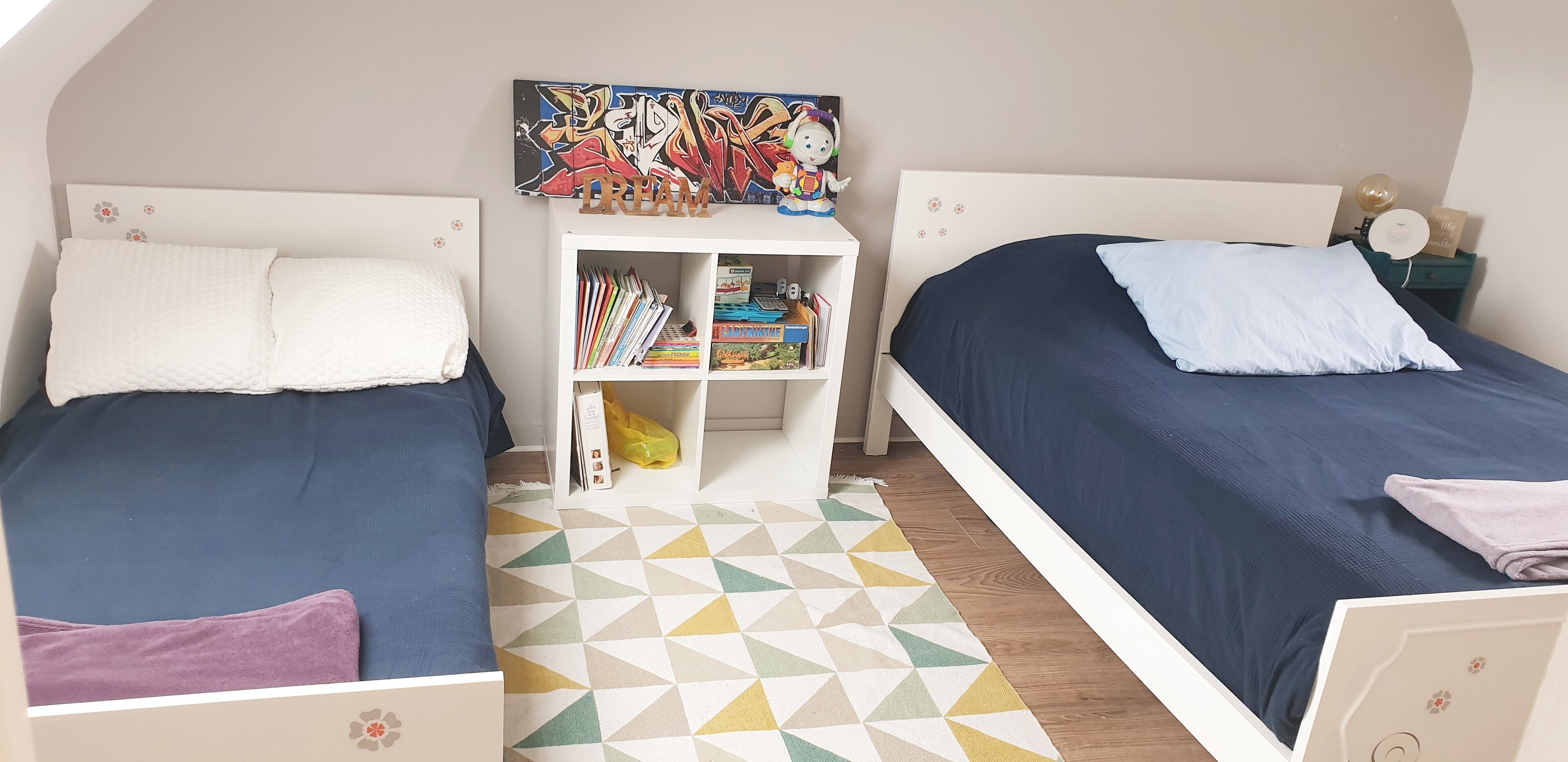 Ein Schlafzimmer mit zwei Betten, einem Bücherregal und einem farbenfrohen, geometrischen Teppich.
