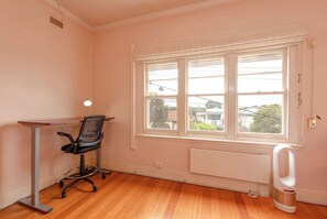 A room with a wooden floor, a desk, a black office chair, a window with a view of houses, and a white radiator. - 3BDR Unit in the Heart of Beautiful Northcote (Northcote South)