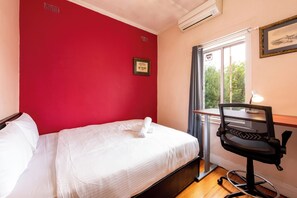 A hotel room with a red wall, a bed with white linens, a desk with a chair, and a window with a view of trees. - 3BDR Unit in the Heart of Beautiful Northcote (Northcote South)