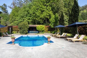 A swimming pool with lounge chairs and umbrellas, surrounded by lush greenery.