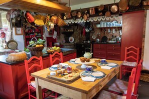A traditional kitchen with wooden cabinets, a dining table set for four, and various kitchen utensils hanging above.