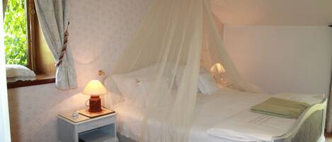 A bedroom with a canopy bed, a bedside table with a lamp, and a chair.