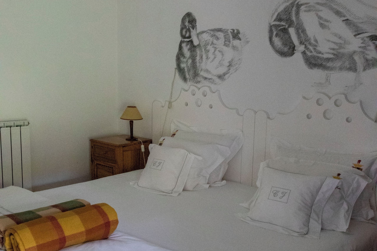 Una cama bien tendida con sábanas blancas, un plaid escocés y un mural en la pared con lechuzas.