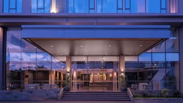 A modern building with a glass facade, a covered entrance, and a staircase leading to the main entrance.