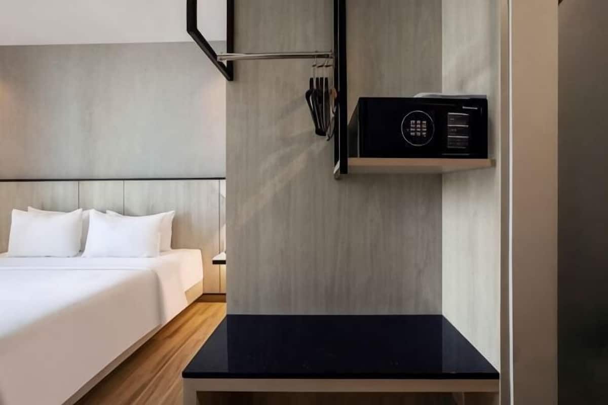 A hotel room with a bed, a black table, a microwave, and a wall-mounted shelf.