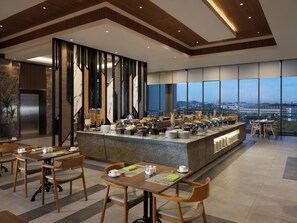 A modern dining area with a buffet, wooden chairs, and a view of the cityscape through large windows. - Hotel Santika Batam (Batam)