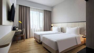 A hotel room with two beds, a desk, a chair, a TV, and a large window with curtains.