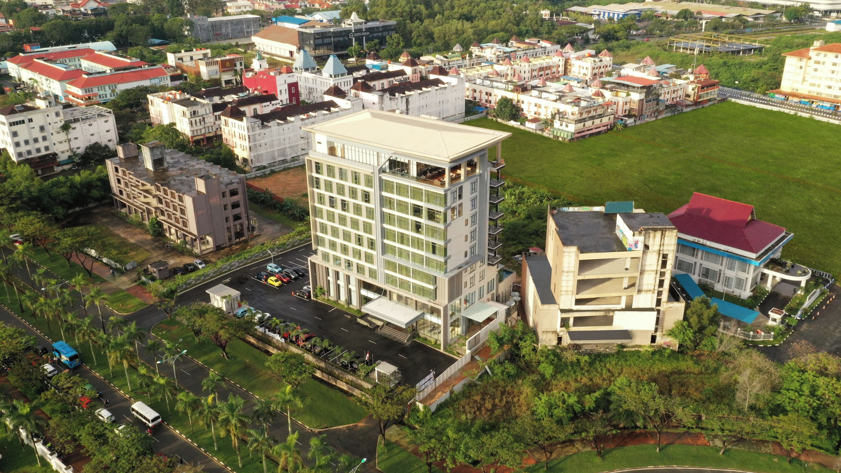 An aerial view of a multi-story hotel with a central courtyard, surrounded by various buildings and greenery.
