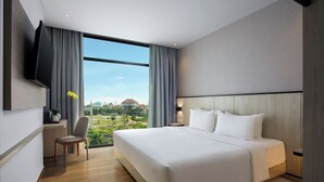 A modern hotel room with a large bed, a flat-screen TV mounted on the wall, a desk with a chair, and a view of a golf course and buildings through large windows. - Hotel Santika Batam (Batam)