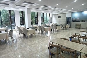 Un vaste espace dédié à la salle à manger, avec des tables et des chaises, de grandes fenêtres et un coin cuisine.