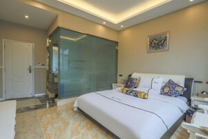 A modern hotel room with a large bed, a glass shower enclosure, and a painting on the wall.