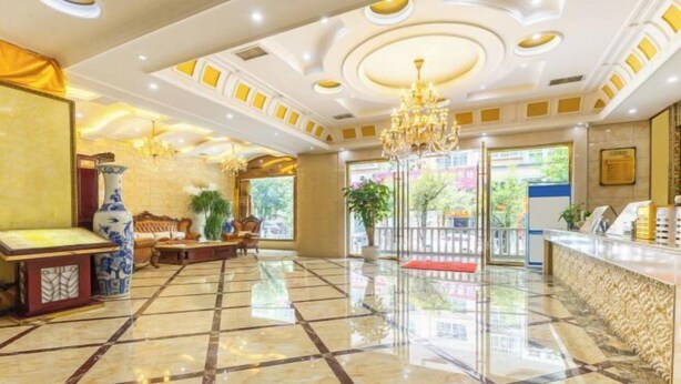 Un vestíbulo de hotel con piso de mármol, mostrador de recepción, candelabro y un amplio ventanal.