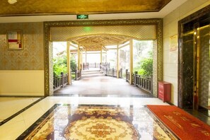 A hotel lobby with a marble floor, a patterned carpet, and a reception desk.