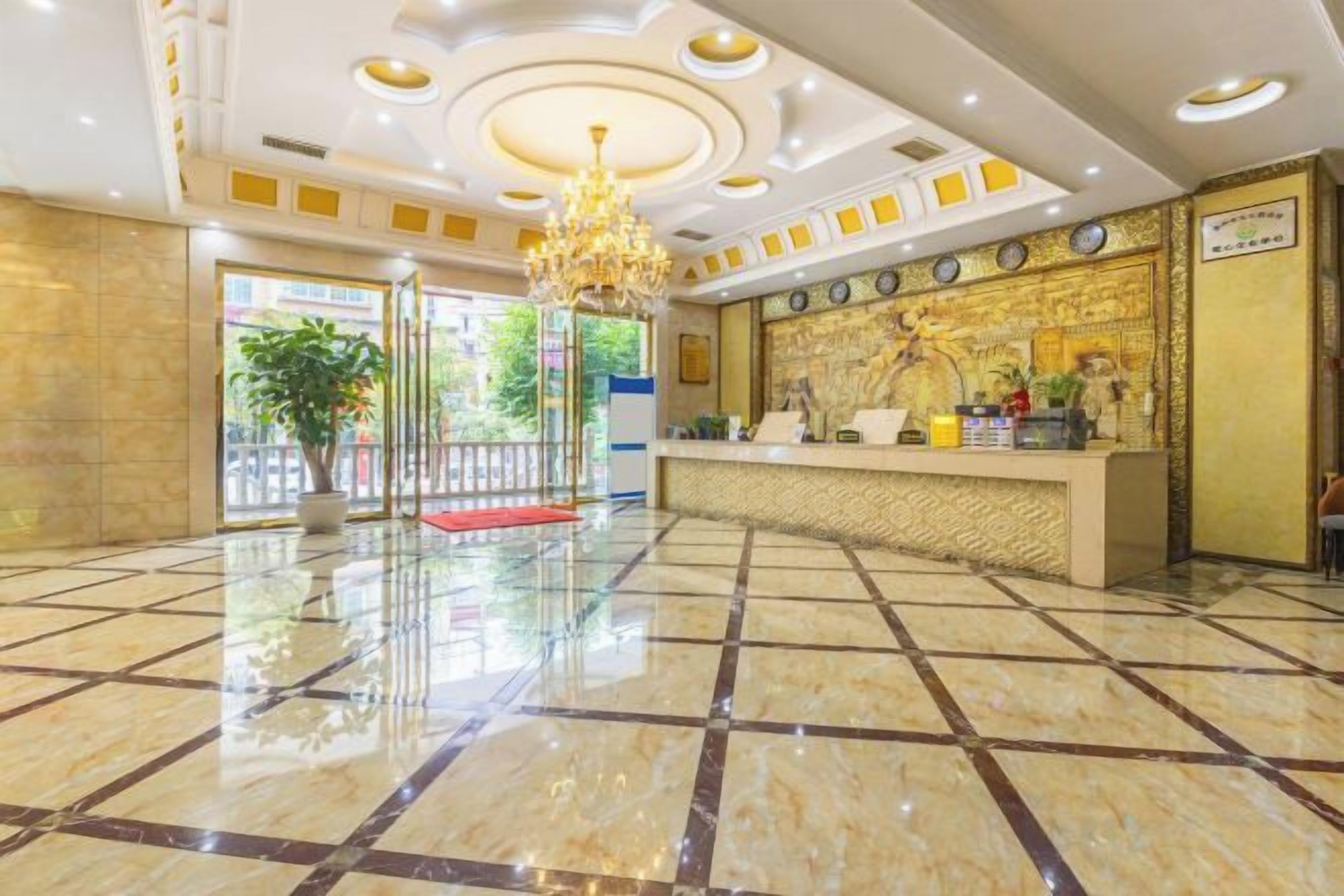 A hotel lobby with a reception desk, a chandelier, and a tiled floor.