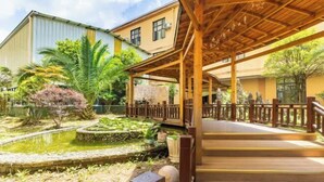 Un espacio al aire libre cubierto con una terraza de madera, un pequeño estanque y vegetación circundante.