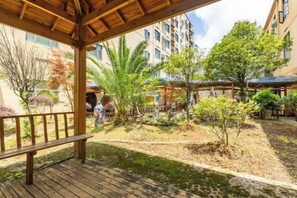 Un espace extérieur abrité, doté d’une terrasse en bois, entouré de verdure et de bâtiments.