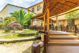 Un espacio al aire libre techado con piso de madera, un pequeño estanque y un edificio al fondo.