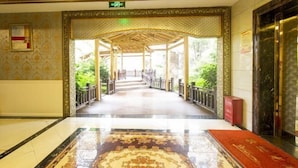 Un vestíbulo de hotel con alfombra estampada, un dosel de madera en la entrada y vistas al jardín exterior.