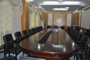Un salón de conferencias con una larga mesa y sillas, una pantalla de proyector y una pizarra.