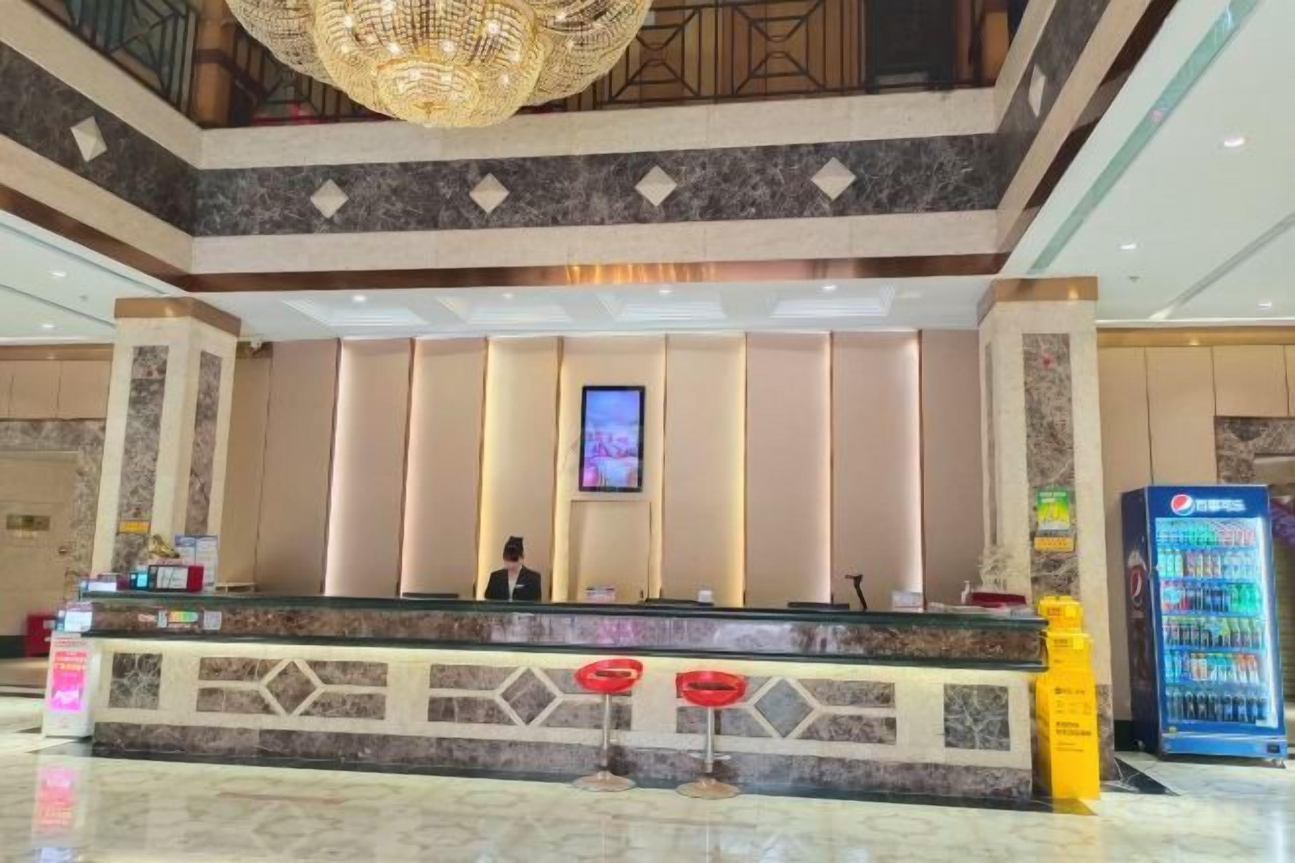 Un espace d’accueil d’hôtel comprenant un comptoir de réception, un écran numérique et un distributeur automatique.
