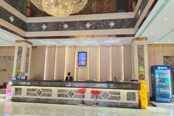 Zona de recepción de hotel con mostrador, pantalla digital y máquina expendedora.