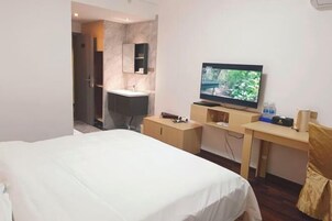 Una habitación de hotel con cama, televisión, escritorio y baño con lavamanos y espejo.