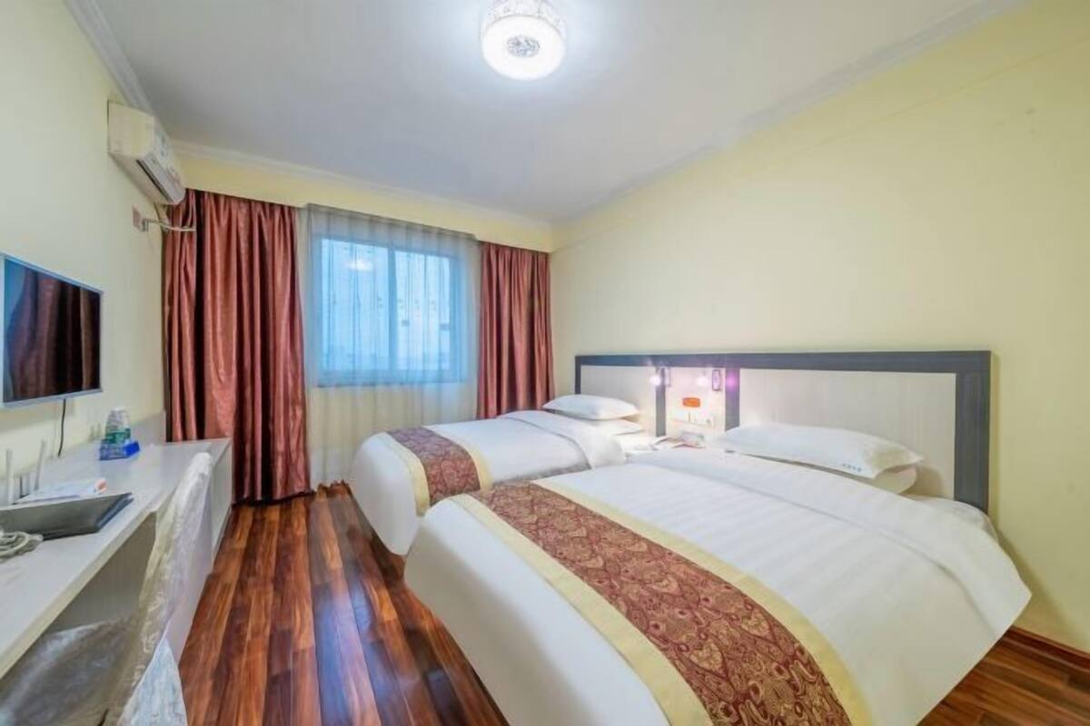 A hotel room with two beds, a desk, a TV, and a window with curtains.