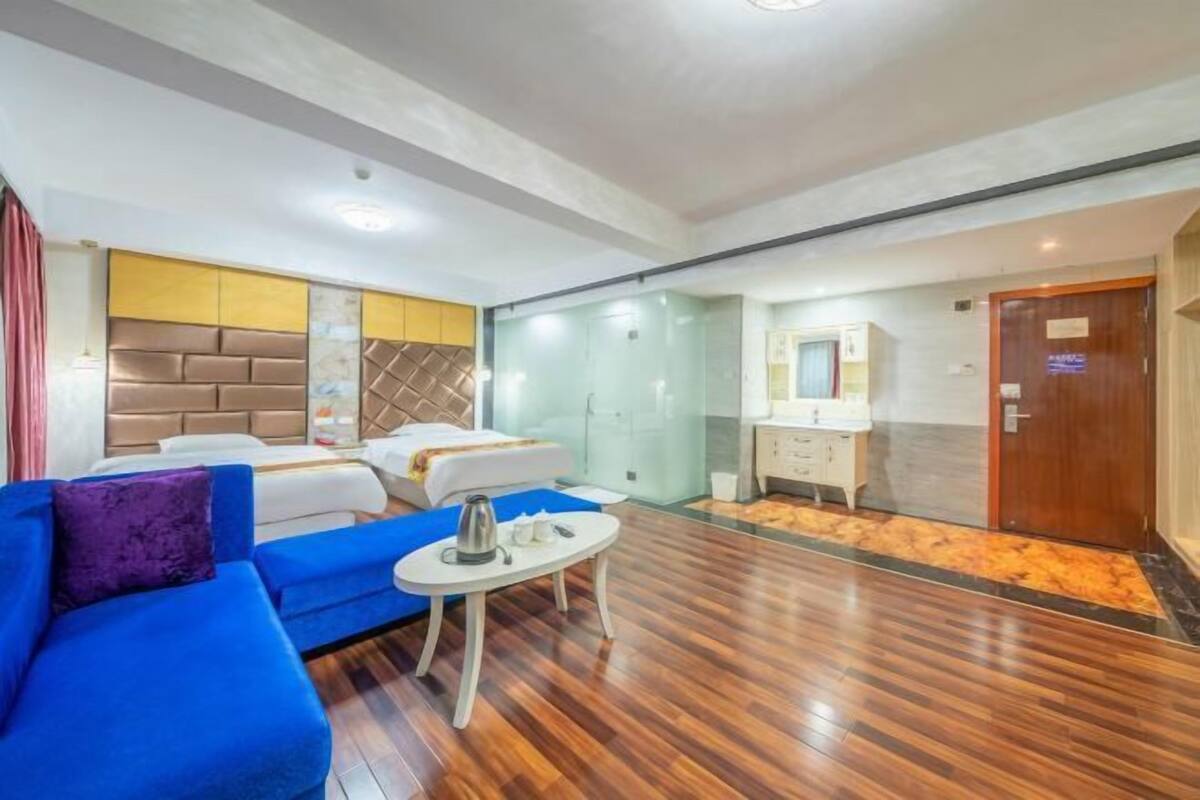 A hotel room with a bed, a blue sofa, a small table, and a bathroom with a mirror and cabinets.