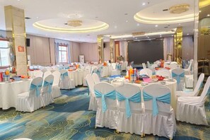 A banquet hall with round tables, white chairs with blue sashes, and a blue carpeted floor. - Laibin Hotel (Laibin)