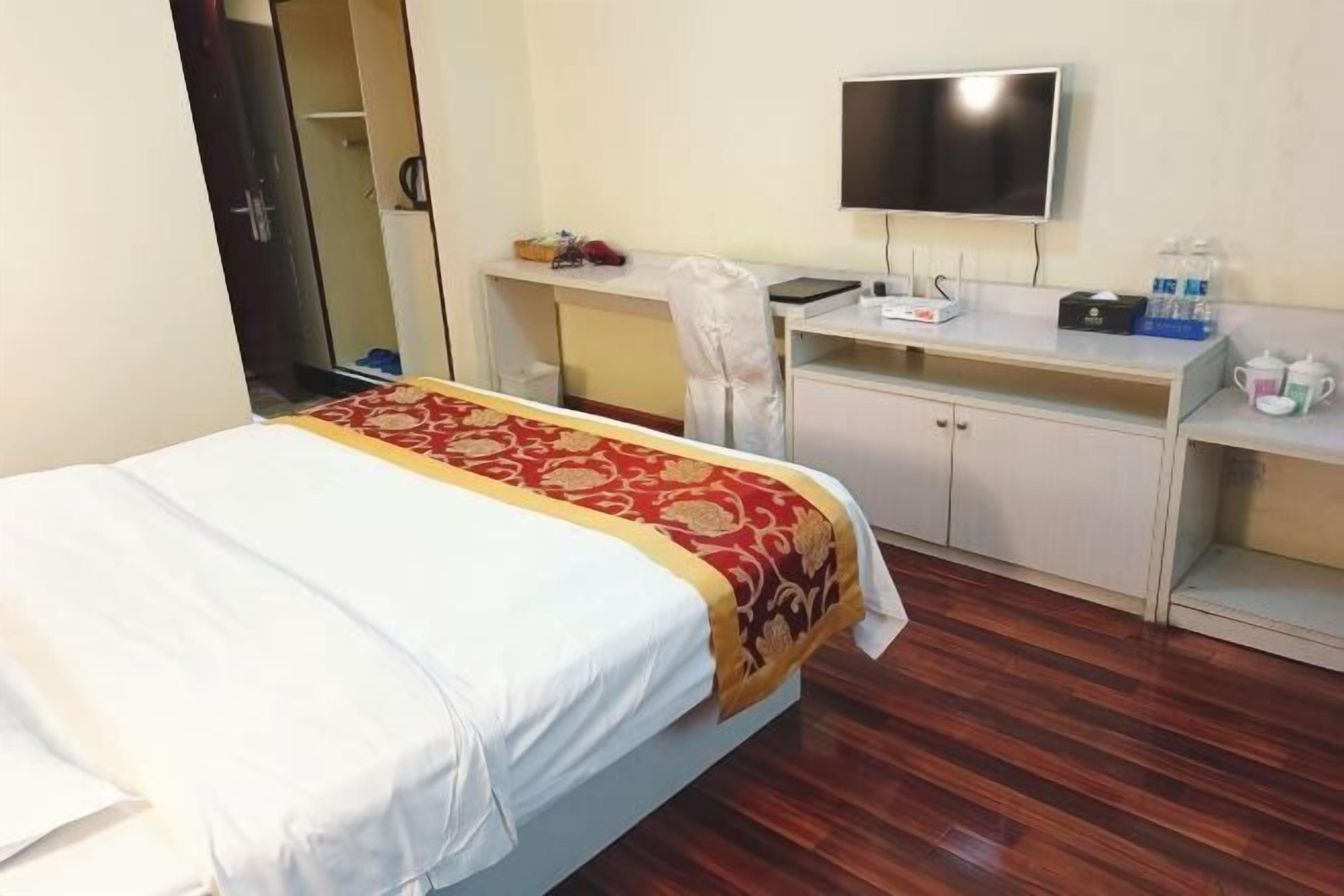 A hotel room with a bed, a desk, a chair, a television, and a wardrobe.