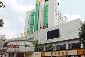 Un edificio de varios pisos con una estructura vertical destacada, una gran pantalla digital y varios rótulos comerciales.