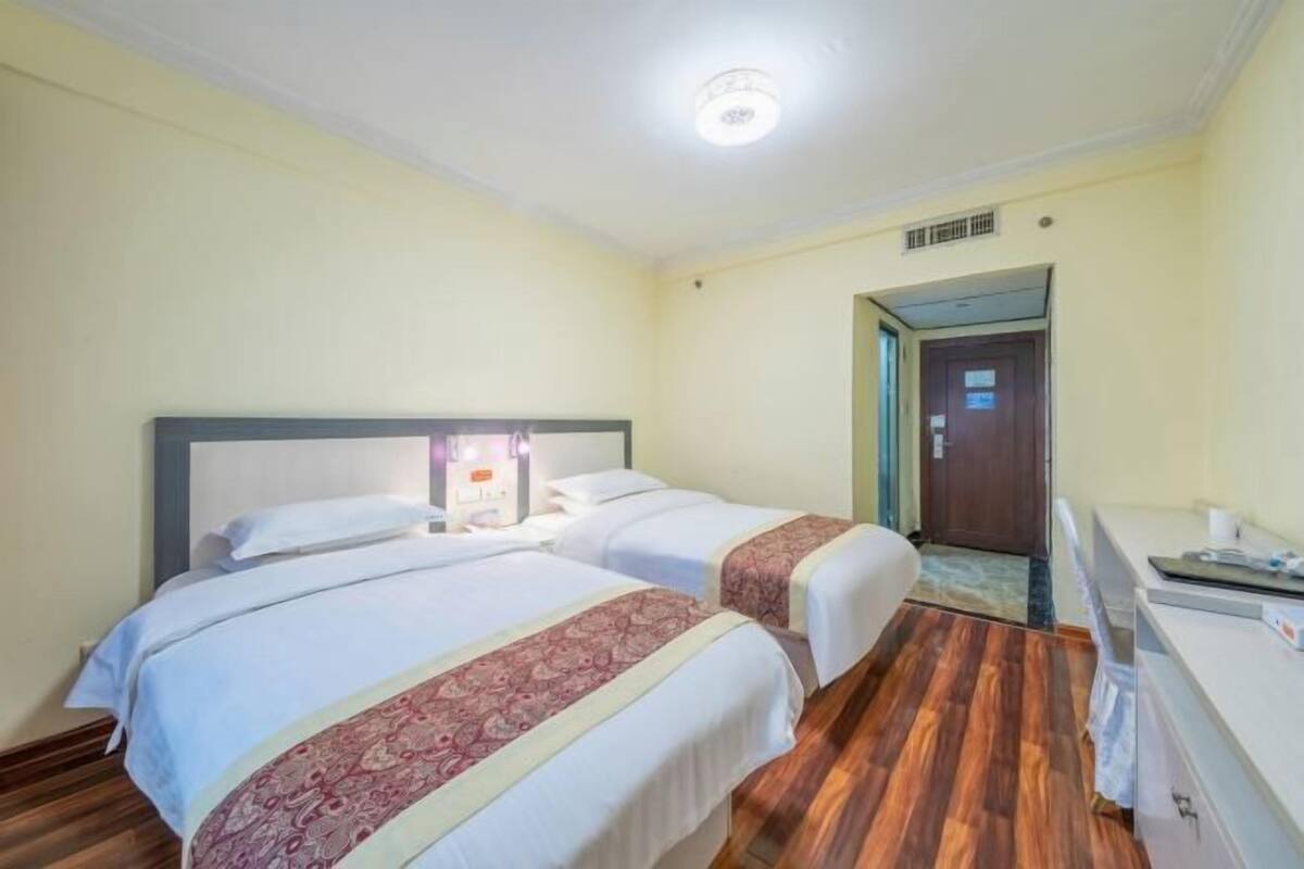 A hotel room with two beds, a desk, and a door leading to another room.